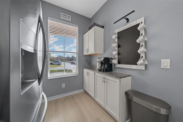 kitchen with stainless steel fridge, white cabinetry, light wood-style flooring, and baseboards