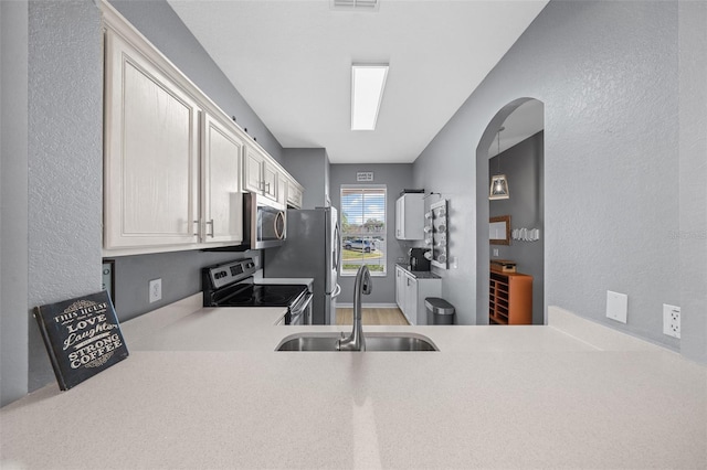 kitchen featuring a sink, stainless steel appliances, light countertops, white cabinets, and a textured wall