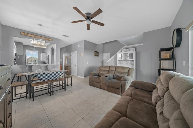 living room featuring light tile patterned flooring, visible vents, ceiling fan with notable chandelier, and baseboards