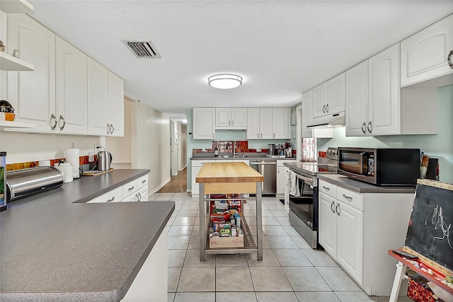 kitchen with dark countertops, visible vents, appliances with stainless steel finishes, light tile patterned flooring, and under cabinet range hood