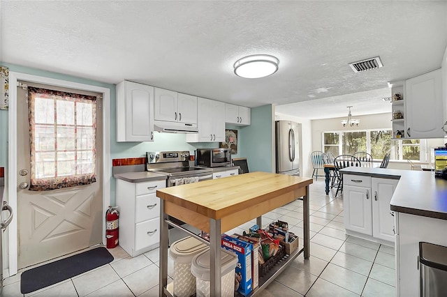 kitchen with light tile patterned flooring, under cabinet range hood, stainless steel appliances, visible vents, and white cabinets