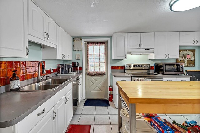 kitchen with light tile patterned floors, stainless steel appliances, a sink, wood counters, and under cabinet range hood