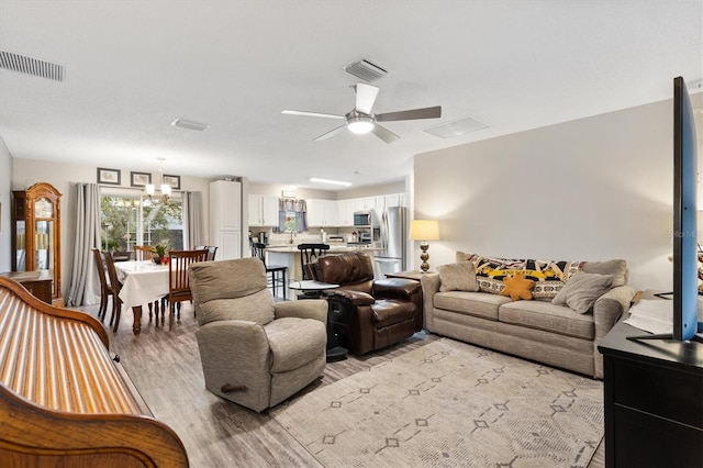 living room featuring ceiling fan with notable chandelier, light wood-style flooring, and visible vents