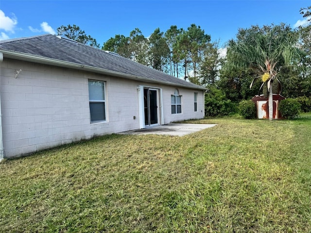 back of house featuring a storage shed, concrete block siding, an outbuilding, a yard, and a patio area