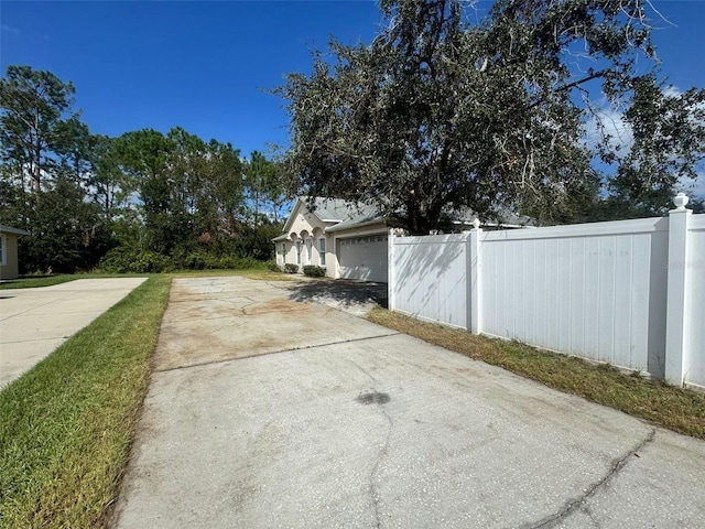 exterior space with a garage, concrete driveway, and fence