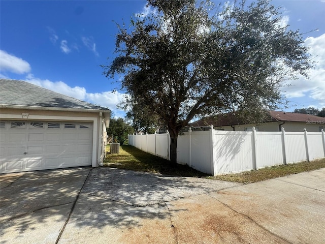 garage featuring driveway, central AC, and fence