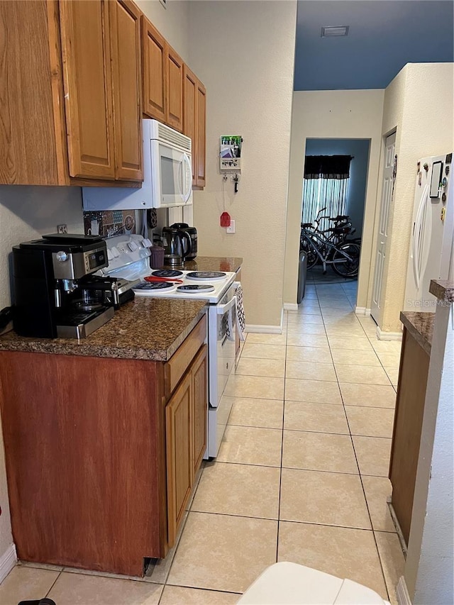 kitchen featuring brown cabinetry, dark countertops, white appliances, and light tile patterned floors