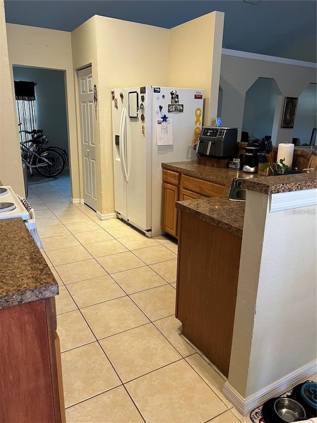 kitchen with light tile patterned floors, white fridge with ice dispenser, dark countertops, and a peninsula