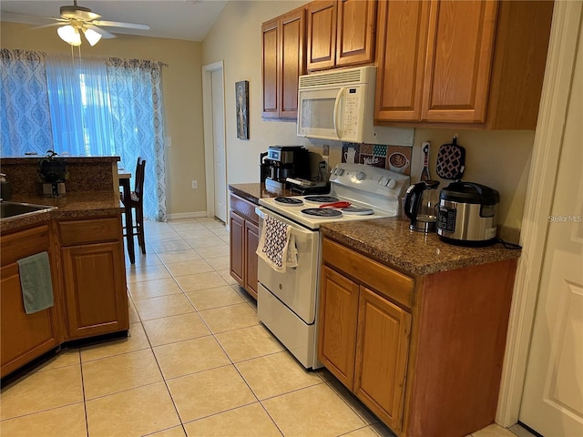 kitchen with brown cabinetry, dark countertops, white appliances, and light tile patterned flooring