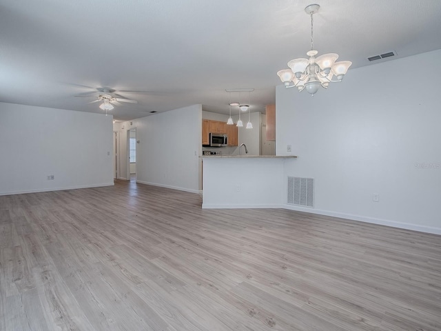 unfurnished living room with ceiling fan with notable chandelier, light wood finished floors, visible vents, and baseboards