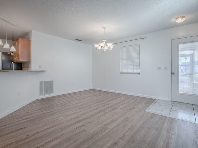 unfurnished dining area featuring light wood-type flooring, baseboards, visible vents, and a textured ceiling