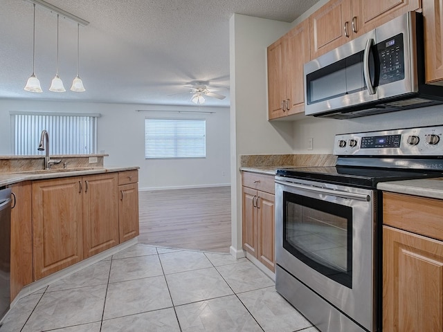 kitchen featuring light tile patterned floors, appliances with stainless steel finishes, a ceiling fan, a sink, and a textured ceiling