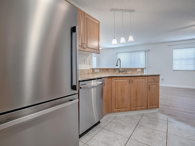 kitchen featuring light tile patterned floors, appliances with stainless steel finishes, a sink, a textured ceiling, and a peninsula