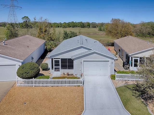 ranch-style house featuring concrete driveway, roof with shingles, fence, and an attached garage