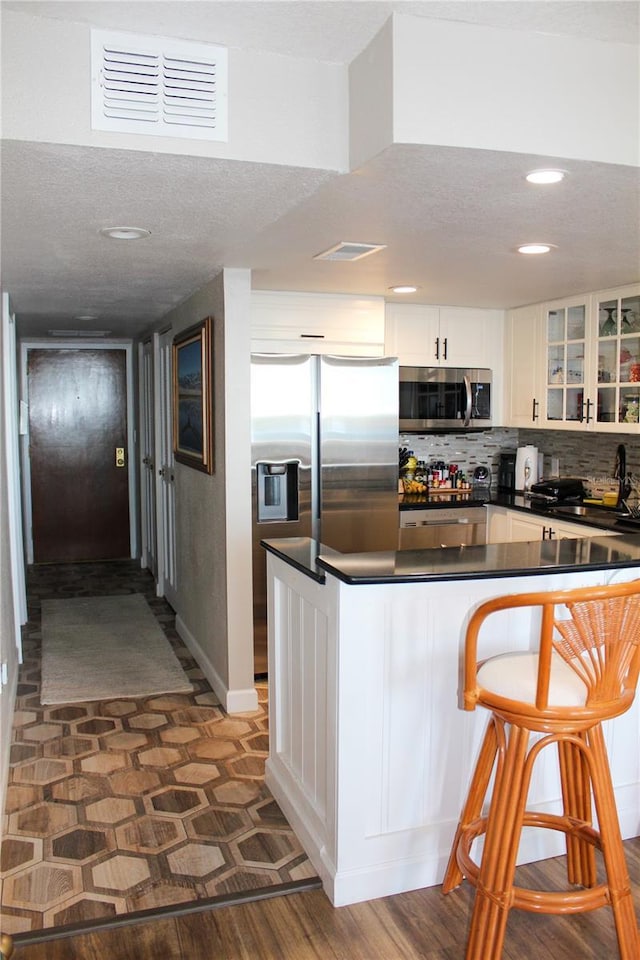 kitchen featuring stainless steel appliances, visible vents, white cabinets, dark countertops, and glass insert cabinets