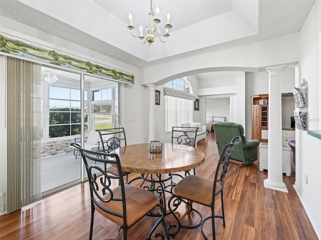 dining area featuring arched walkways, a textured ceiling, wood finished floors, a tray ceiling, and decorative columns