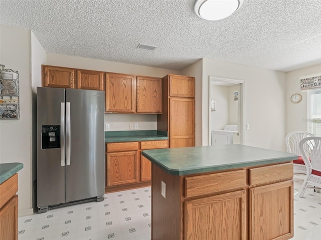 kitchen featuring stainless steel refrigerator with ice dispenser, light floors, visible vents, brown cabinetry, and washing machine and dryer