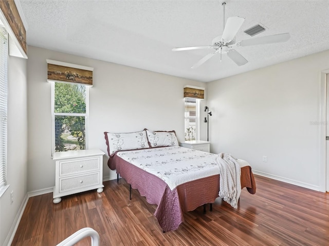 bedroom featuring a textured ceiling, wood finished floors, visible vents, baseboards, and a ceiling fan