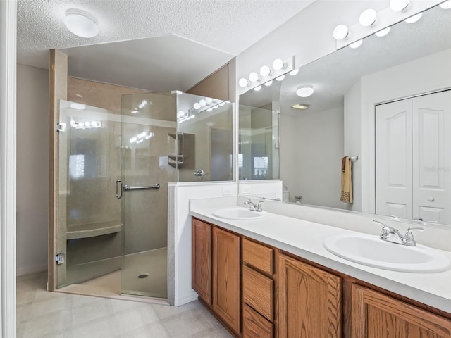 full bath with a textured ceiling, double vanity, a stall shower, and a sink