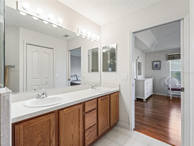 full bathroom featuring double vanity, a textured ceiling, visible vents, and a sink