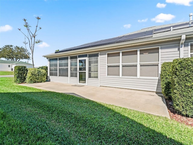 rear view of house with a yard, roof mounted solar panels, a patio, and a sunroom