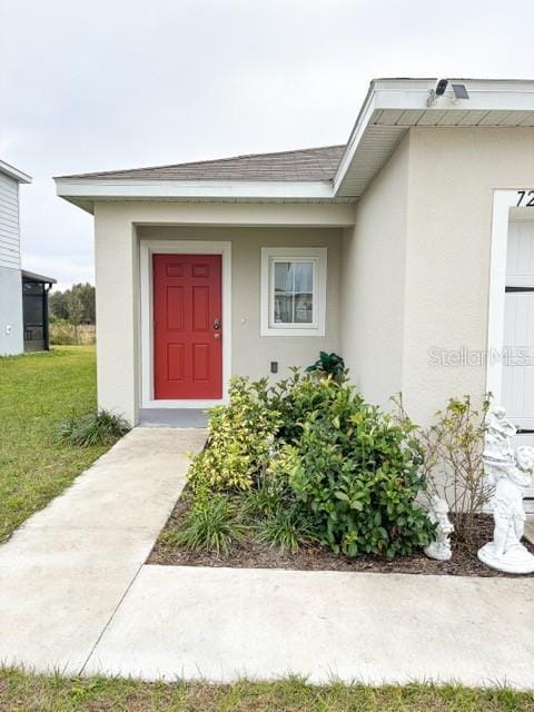 entrance to property with roof with shingles, a lawn, and stucco siding