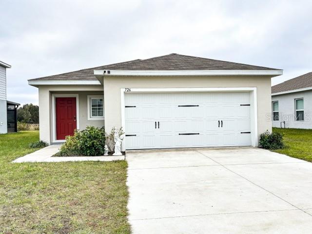 ranch-style home featuring a garage, concrete driveway, a front lawn, and stucco siding