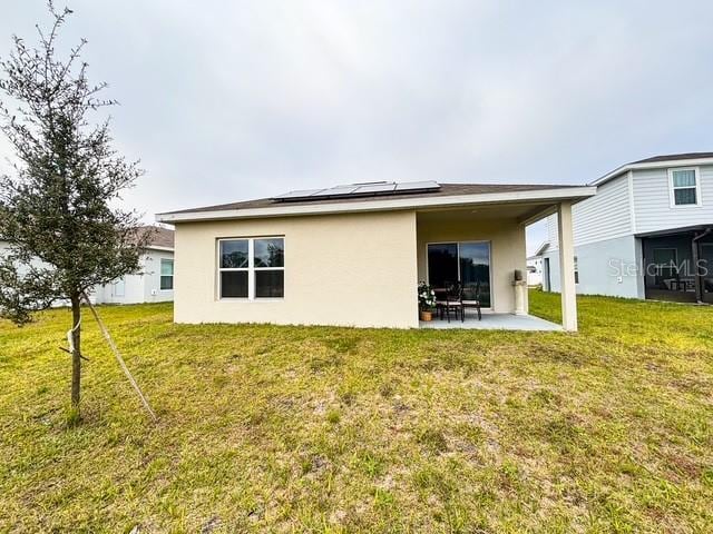 back of house featuring a lawn, a patio area, roof mounted solar panels, and stucco siding