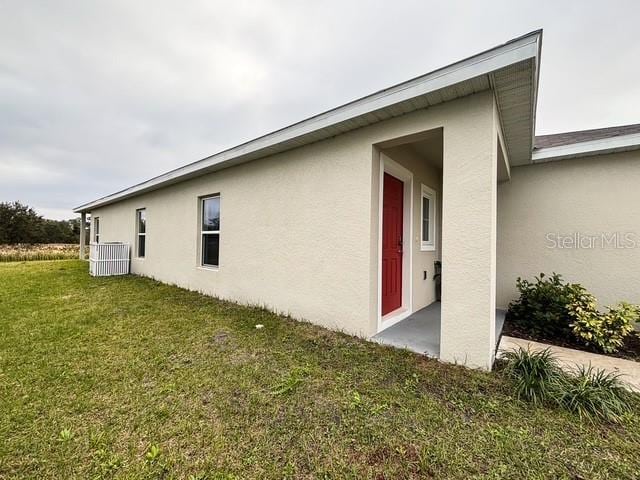 view of property exterior with central AC unit, a lawn, and stucco siding