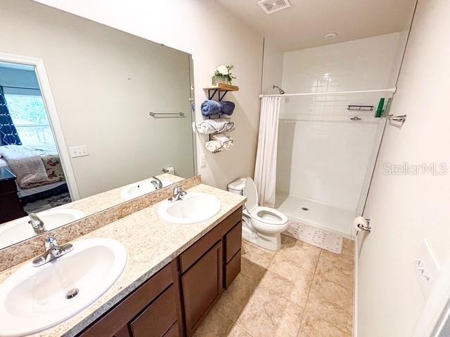 ensuite bathroom featuring toilet, a stall shower, visible vents, and a sink