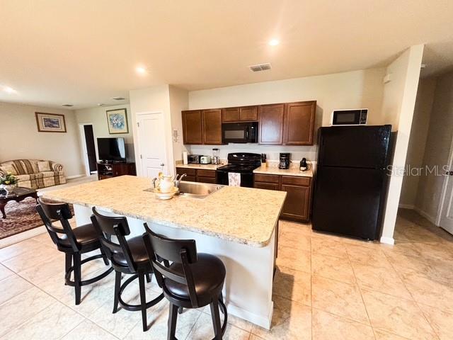 kitchen featuring visible vents, open floor plan, black appliances, an island with sink, and a kitchen breakfast bar