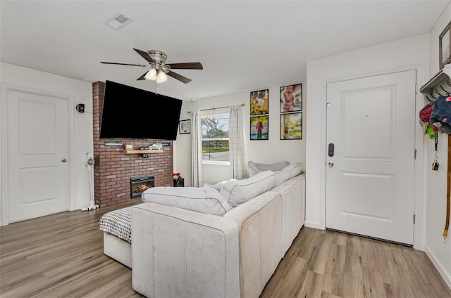 living area with light wood-style flooring, a fireplace, visible vents, and ceiling fan