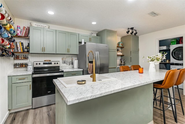 kitchen featuring stainless steel appliances, stacked washer / drying machine, green cabinets, light wood-type flooring, and open shelves