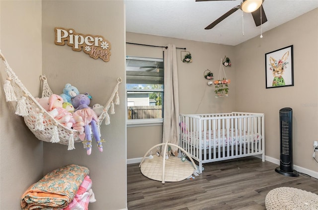 bedroom featuring a nursery area, ceiling fan, baseboards, and wood finished floors