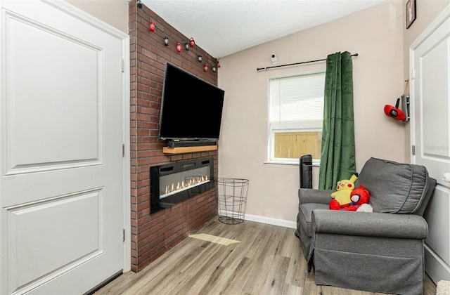 sitting room featuring a brick fireplace, baseboards, and light wood-style floors