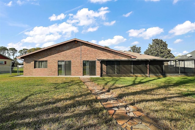 back of house featuring brick siding, a lawn, fence, and a sunroom