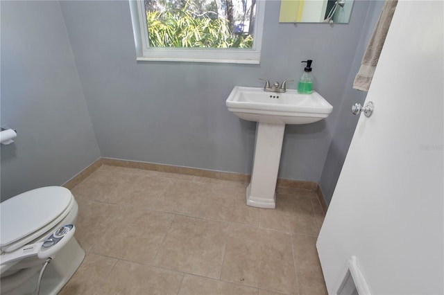 half bathroom featuring toilet, tile patterned flooring, baseboards, and a sink