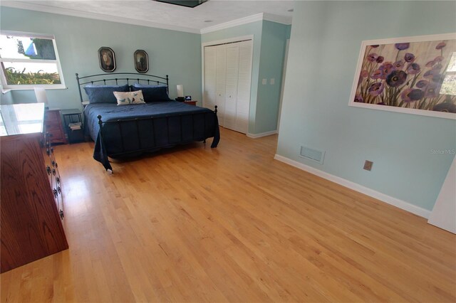 bedroom with crown molding, light wood finished floors, a closet, visible vents, and baseboards