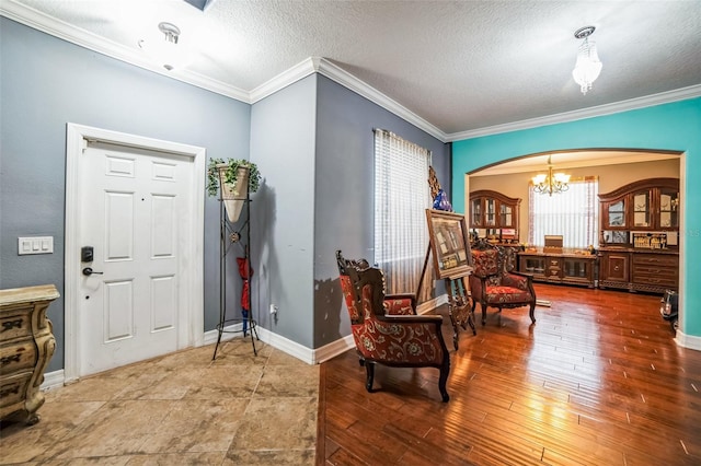 entrance foyer featuring a textured ceiling, arched walkways, wood finished floors, baseboards, and crown molding