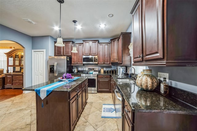 kitchen with visible vents, a kitchen island, dark stone countertops, stainless steel appliances, and a sink