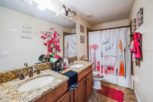 bathroom featuring double vanity, a textured ceiling, toilet, and a sink