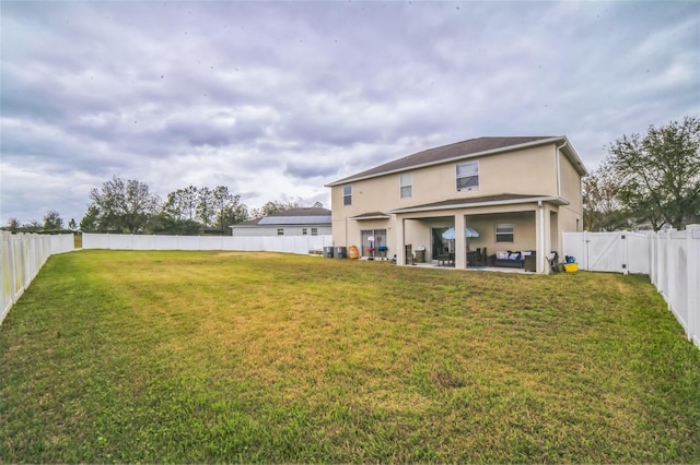 rear view of house featuring a fenced backyard, a yard, a gate, stucco siding, and a patio area