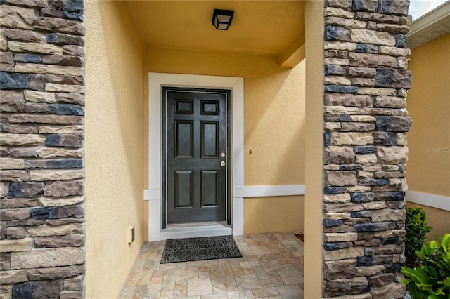 view of exterior entry featuring stone siding and stucco siding