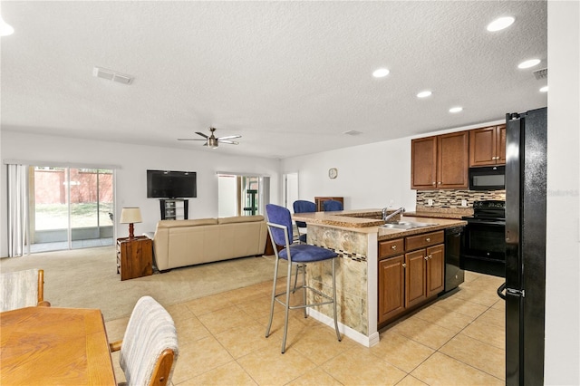 kitchen with a breakfast bar, visible vents, open floor plan, a sink, and black appliances