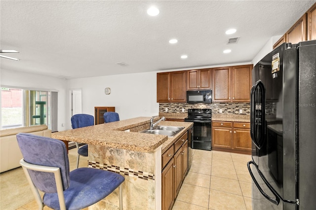 kitchen featuring a sink, a kitchen breakfast bar, open floor plan, backsplash, and black appliances