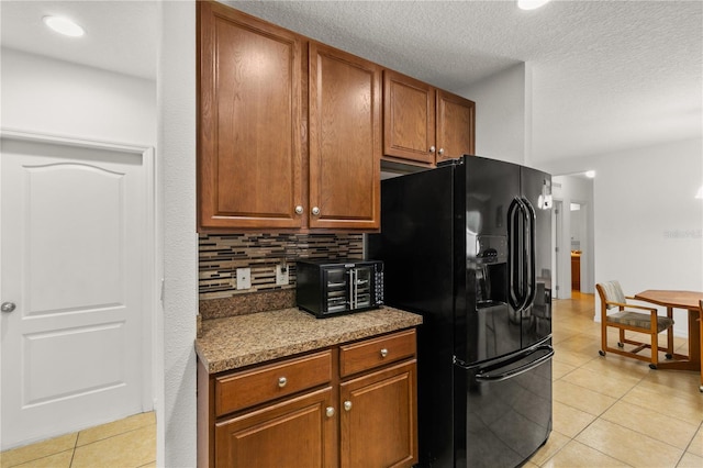 kitchen featuring light tile patterned floors, tasteful backsplash, black refrigerator with ice dispenser, brown cabinetry, and a textured ceiling