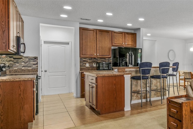 kitchen featuring visible vents, a kitchen island, stainless steel electric range, a kitchen bar, and black fridge