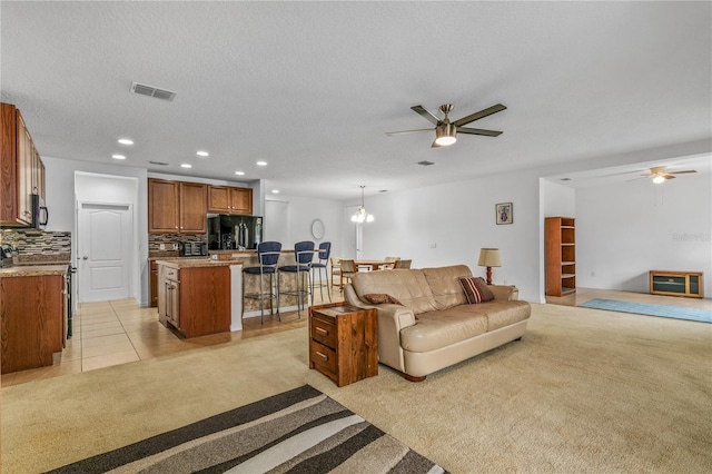 living area with ceiling fan, visible vents, and light colored carpet