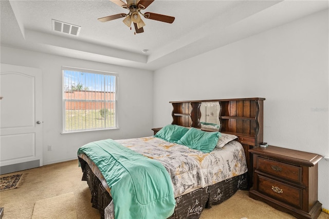 bedroom featuring visible vents, a ceiling fan, light colored carpet, a tray ceiling, and a textured ceiling