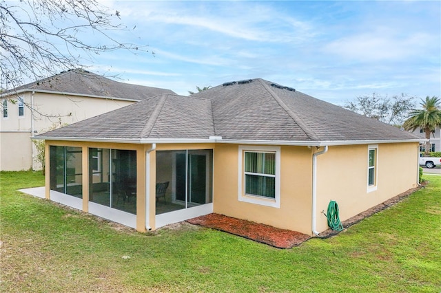 back of property featuring a sunroom, a shingled roof, a lawn, and stucco siding